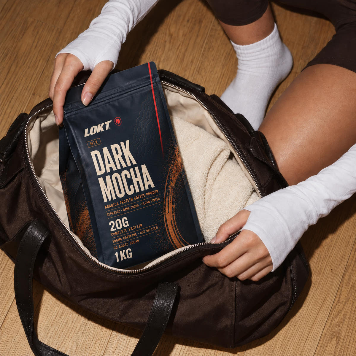 LOKT Dark Mocha protein coffee packed in a brown gym bag on a continuous oak floor