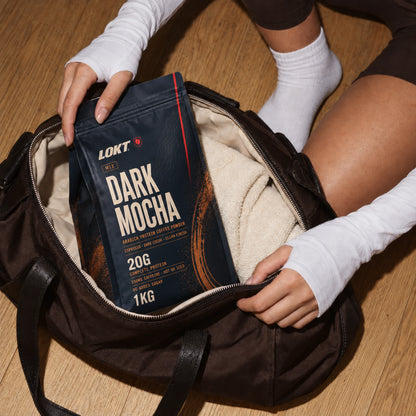LOKT Dark Mocha protein coffee packed in a brown gym bag on a continuous oak floor