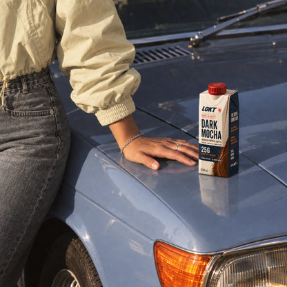 A LOKT READY Dark Mocha 330mL carton on a slate blue car beside a resting hand
