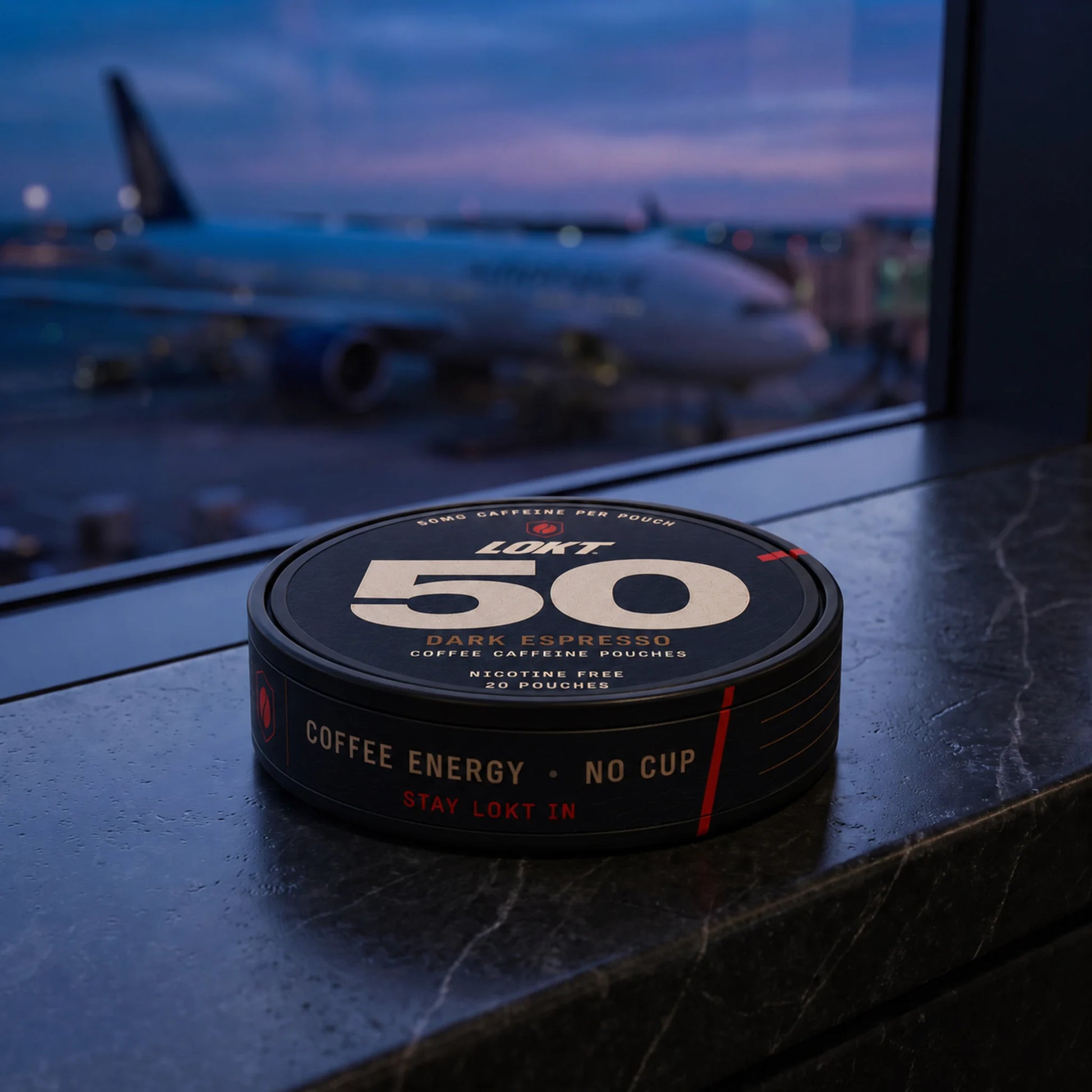 A LOKT 50 Dark Espresso tin on an airport gate ledge at blue hour
