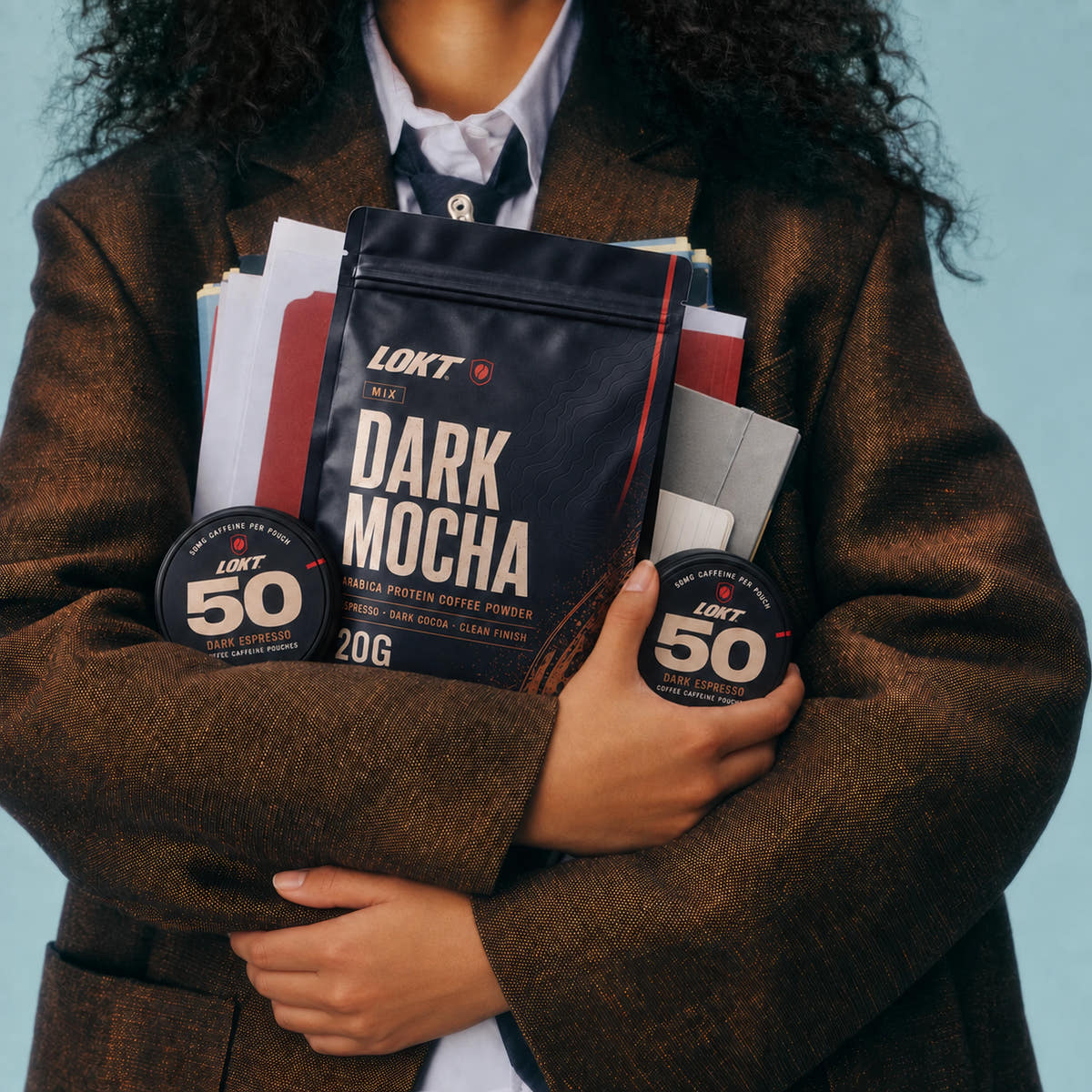 A woman in a brown blazer holds LOKT MIX Dark Mocha and closed Dark Espresso tins with her notebooks