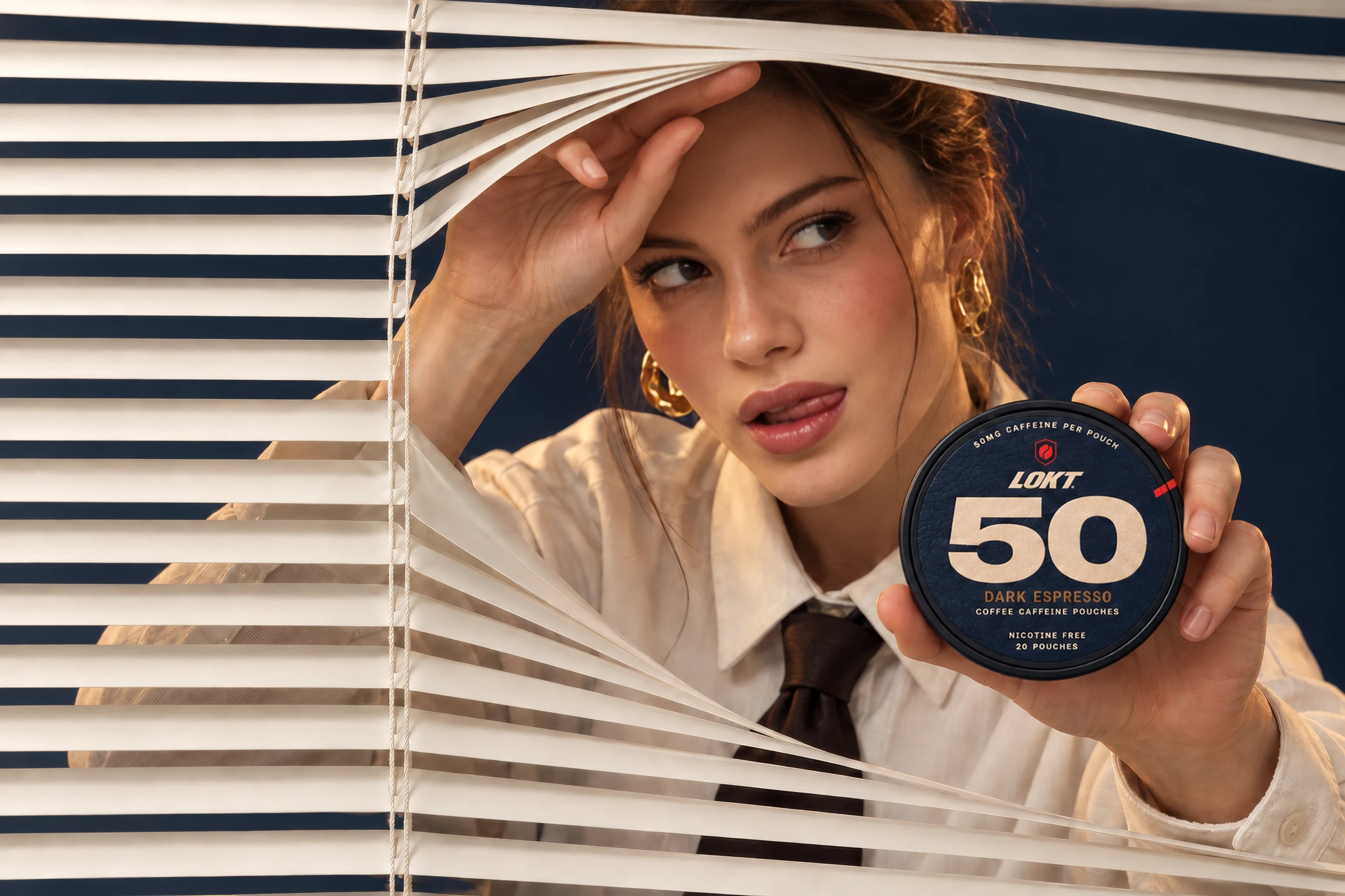 A woman peeks through cream window blinds, holding up a LOKT 50 Dark Espresso coffee pouch tin.