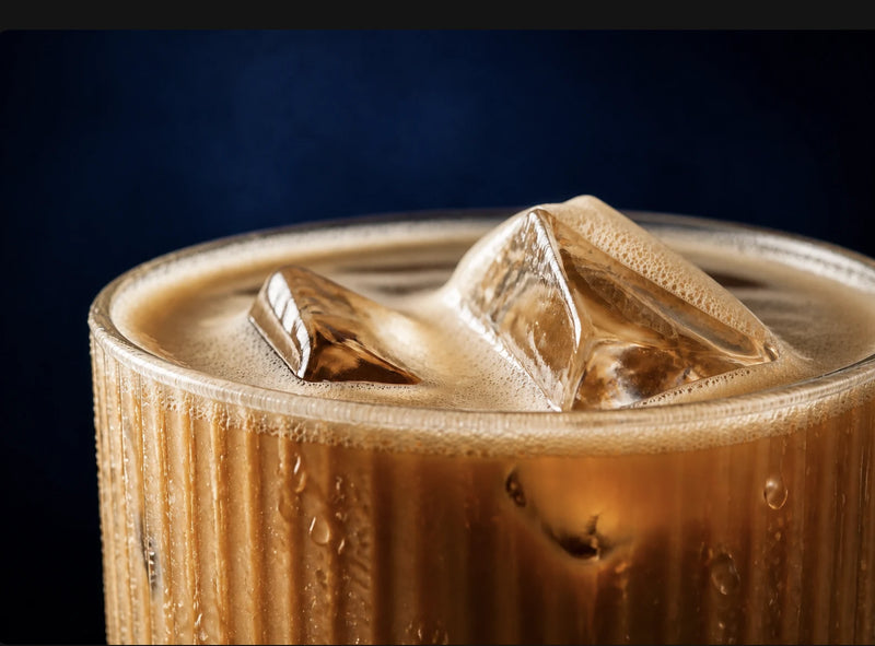 Macro of an iced latte with ice cubes and a fine foam layer in a ribbed glass.